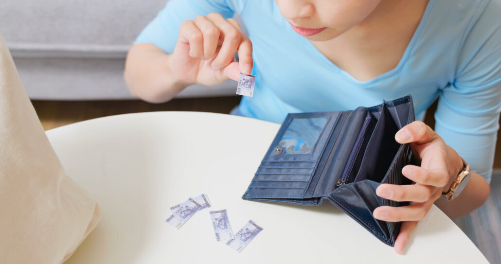 A person in a blue shirt looking closely at tiny banknotes while holding an open, mostly empty wallet