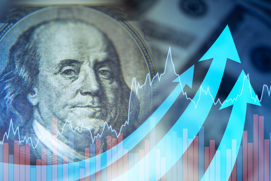 Close-up of Benjamin Franklin on a US $100 bill with financial charts and blue upward arrows representing rising costs and economic trends.