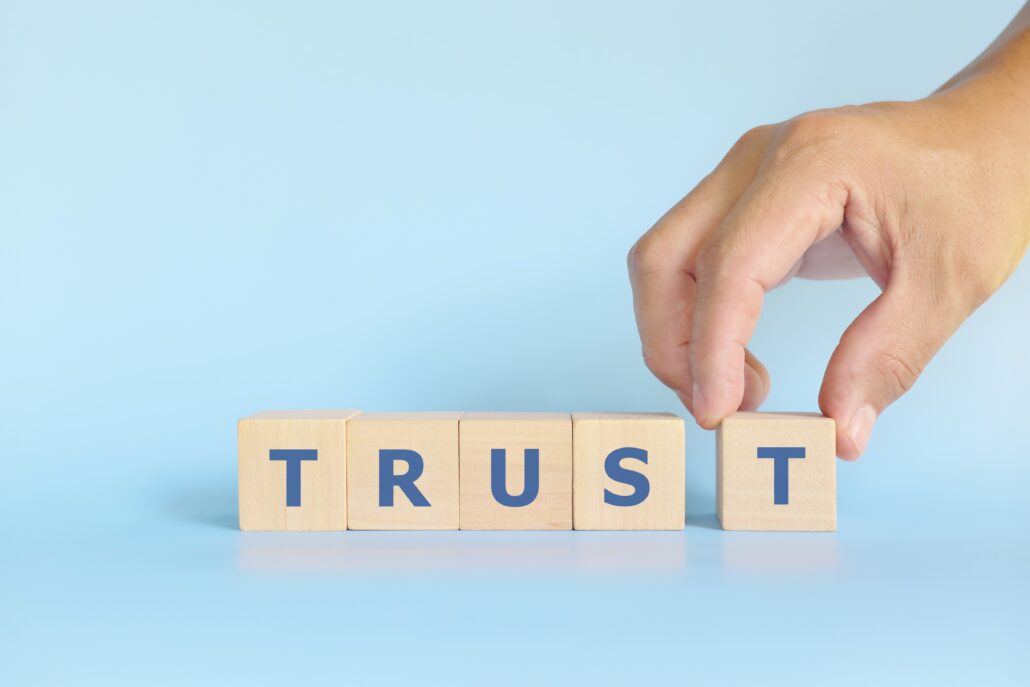 Wooden blocks spelling “TRUST” with a hand placing the final letter T