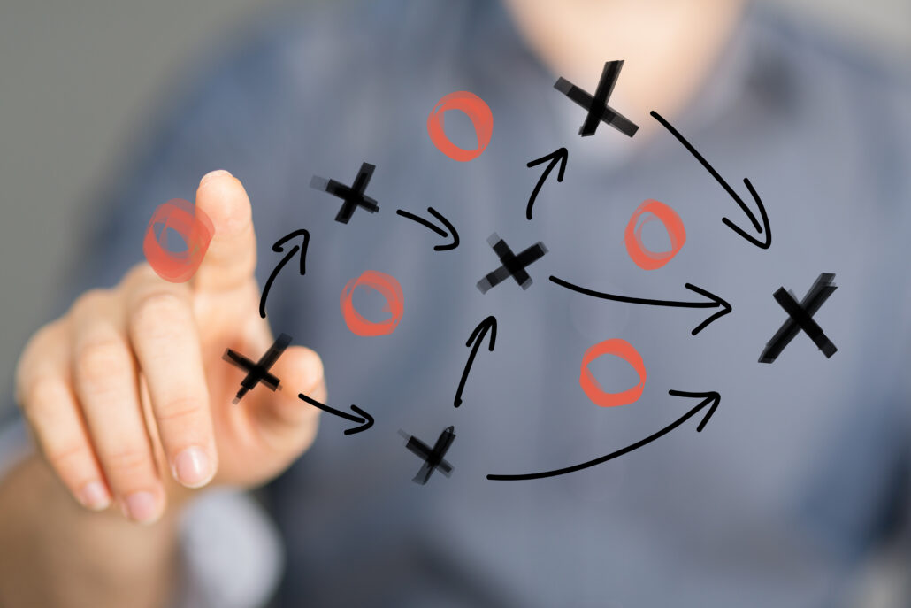 Hand pointing at a transparent board with a simple play diagram of Xs, Os, and arrows.