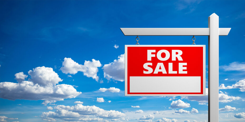 Red “For Sale” sign hanging on a post against a blue sky with white clouds.