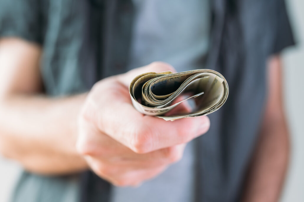 Close-up of a person handing over a small roll of U.S. dollar bills.