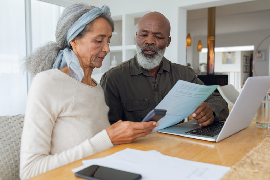 Older couple at a table reviewing a document and using a calculator near a laptop.