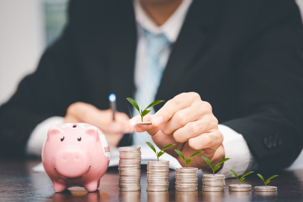 Piggy bank and stacks of coins with small plants growing, representing long-term tax savings and energy-related tax credits for physicians.