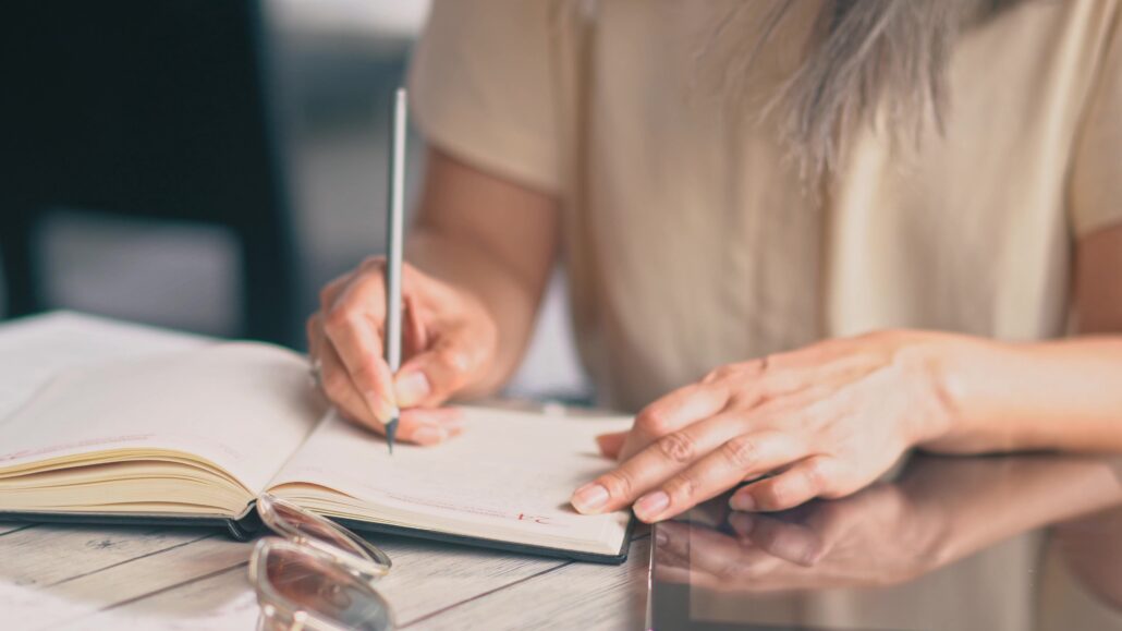 Person writing in a notebook while reviewing expenses, representing equipment planning and Section 179 decisions for physicians.