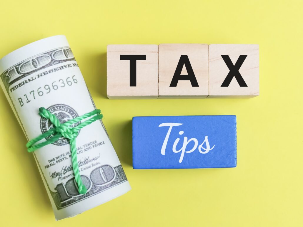 Wood blocks spelling TAX next to a roll of cash and a blue block reading Tips
