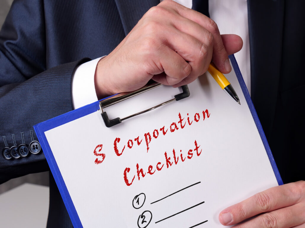 Hand holding a pen over an S Corporation checklist for automating payroll, owner pay, and reimbursements for physician tax planning